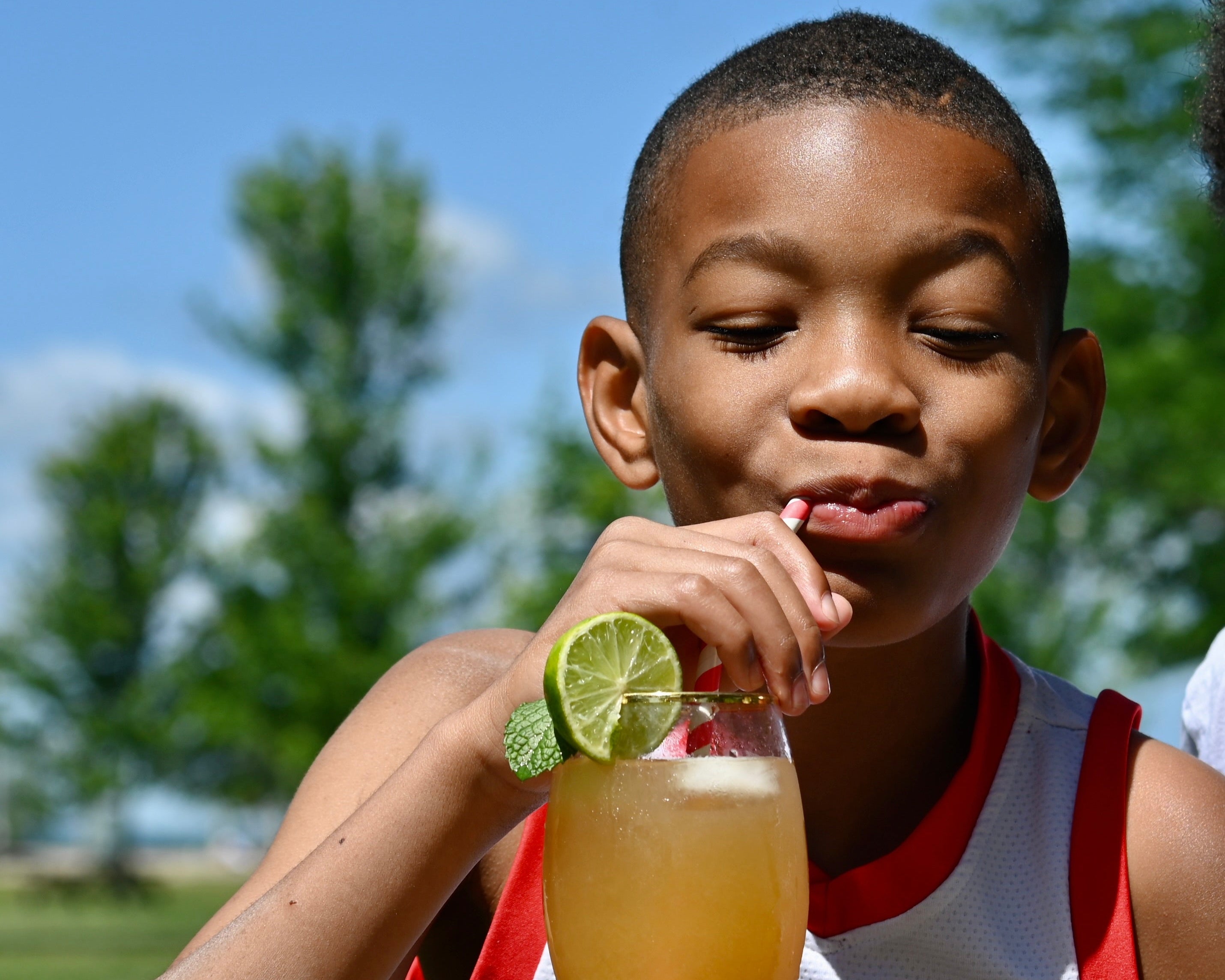 Child drinking a beverage with a lime wedge outdoors